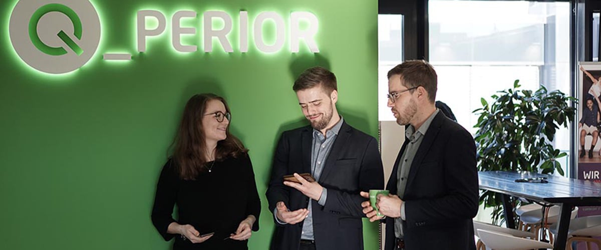 Drei Mitarbeiter stehen vor grüner Wand mit weißem Q-Perior Logo