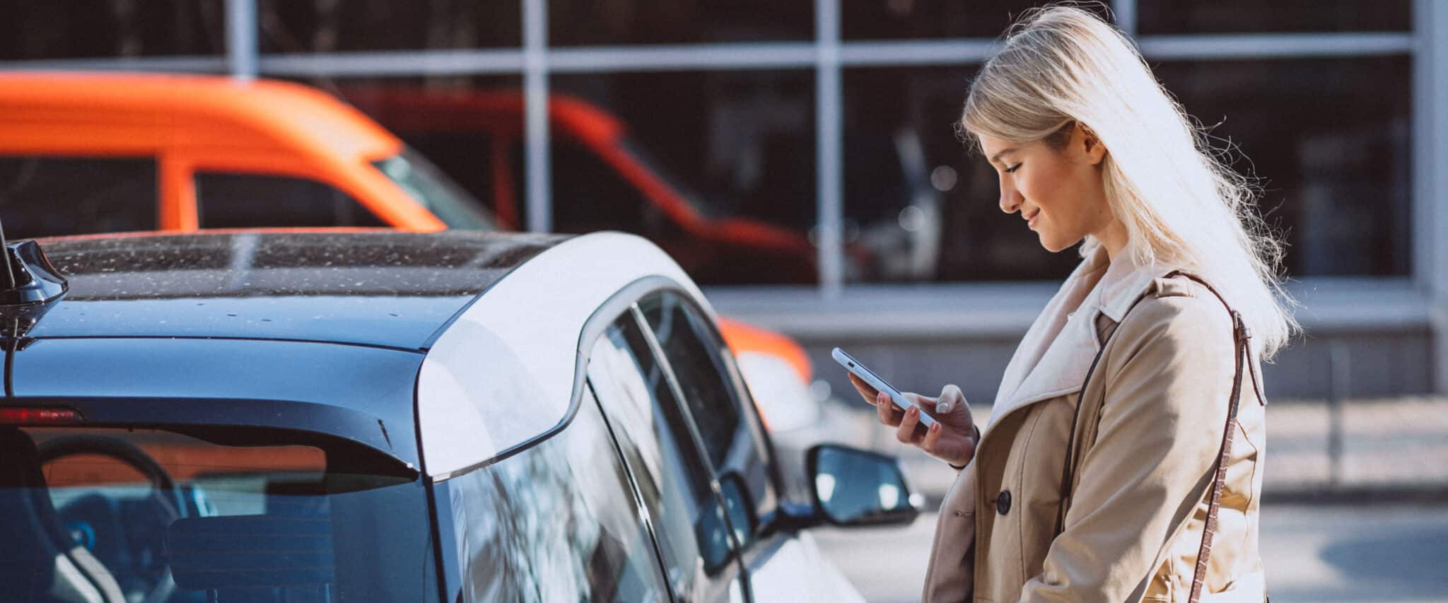 Eine junge blonde Frau schaltet mit dem Handy ihr gemietetes Auto frei.