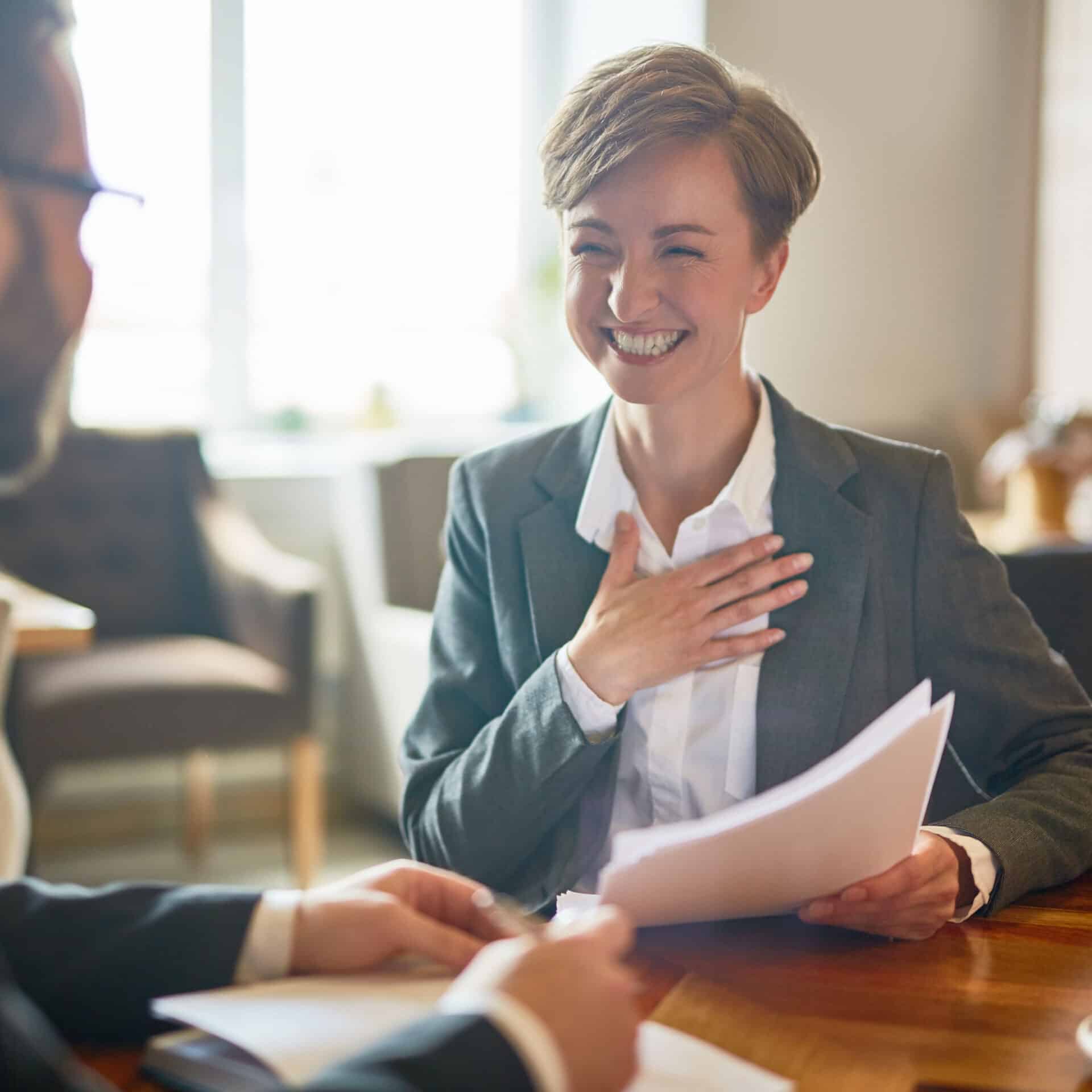 Eine blonde Frau im Anzug freut sich über ihre Gehaltserhöhung im Gespräch mit ihrem Chef.