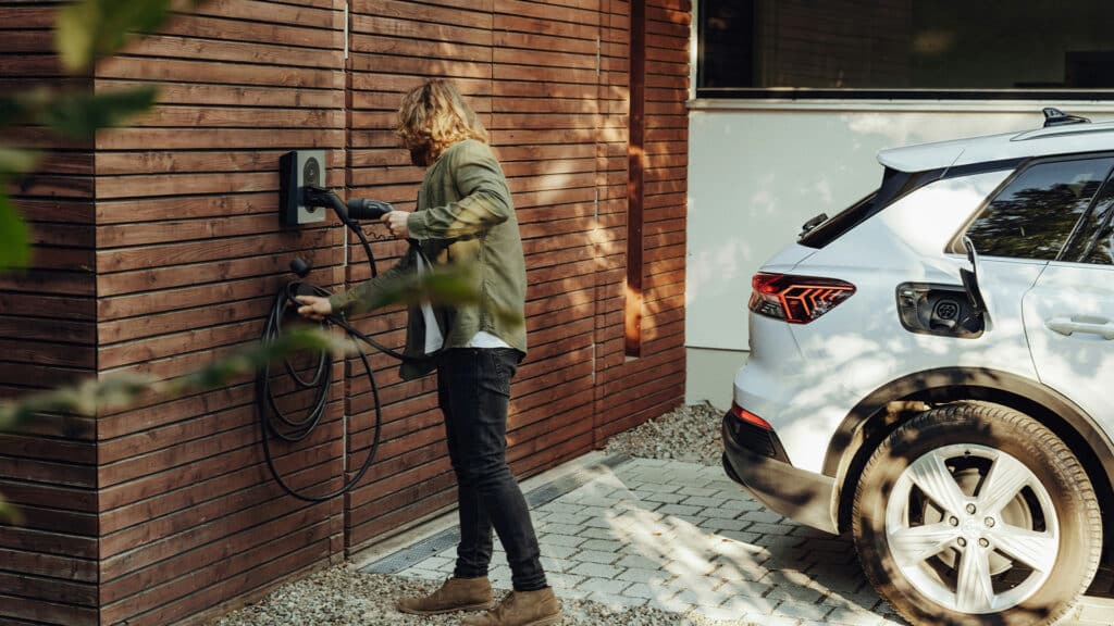 Person lädt weißes E-Auto per Wallbox zuhause