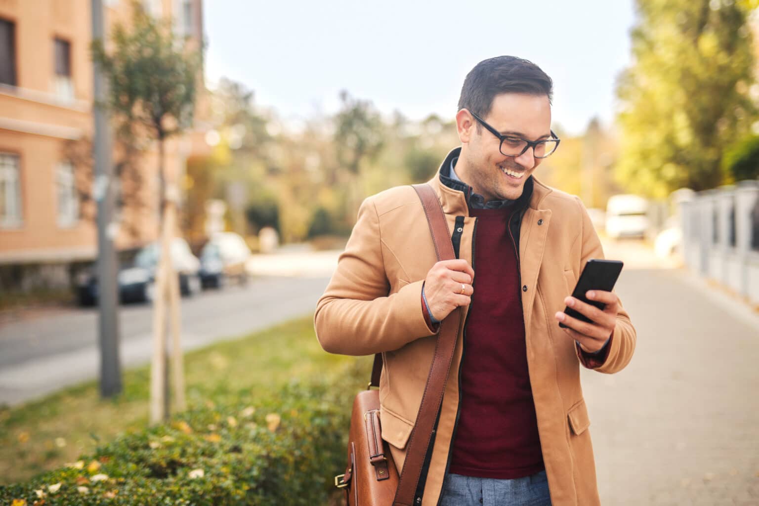Mann auf der Straße schaut lächelnd auf sein Handy