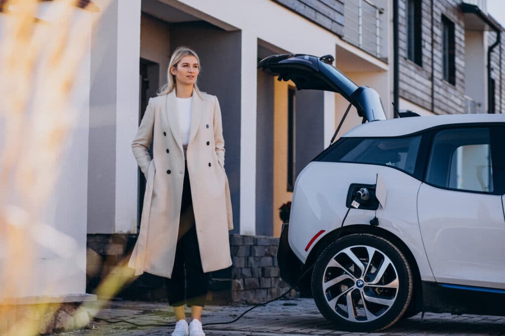 Frau steht vor ihrem Haus und lädt ihr Elektrofahrzeug