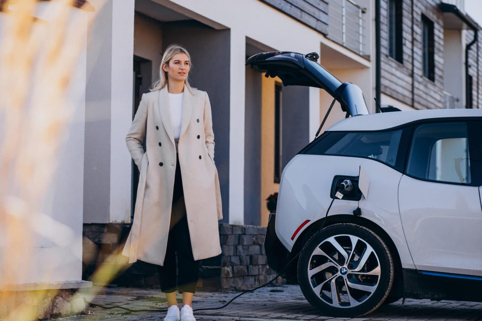 Frau steht vor ihrem Haus und lädt ihr Elektrofahrzeug