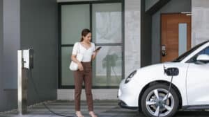 Frau lädt vor einem Haus einen weißen Elektrowagen