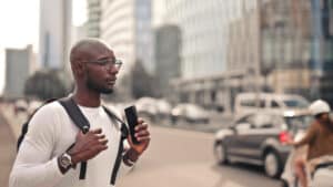 Mann mit Smartphone und Rucksack schaut auf Straße mit Hochhäusern