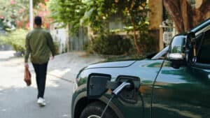 Grünes Auto lädt an Wallbox. Mann geht Richtung Haus